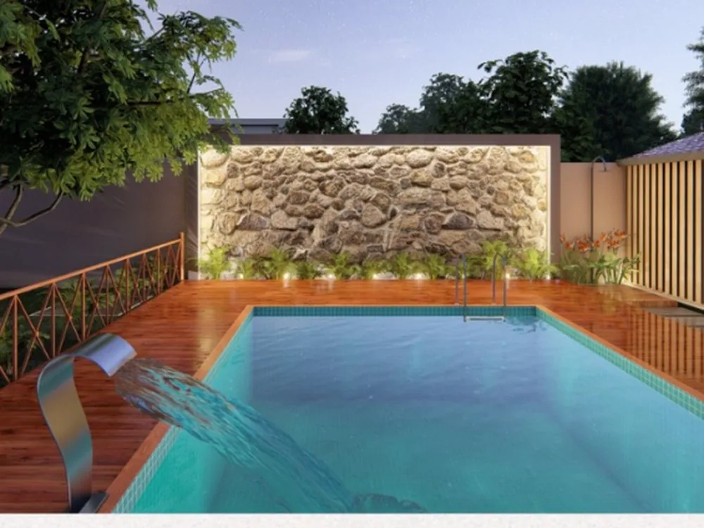 Piscina com cascata, deck de madeira, muro revestido em pedra natural e canteiros iluminados ao anoitecer