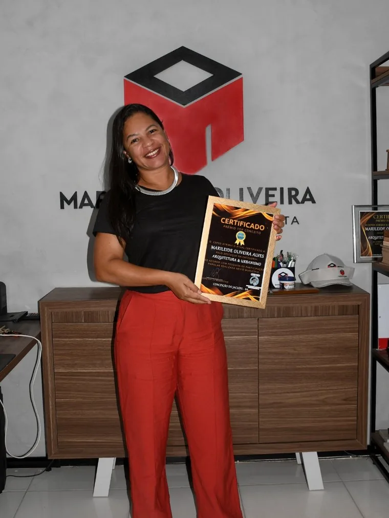 Marileide Oliveira com o certificado do Prêmio Top Conceito em frente à marca do escritório